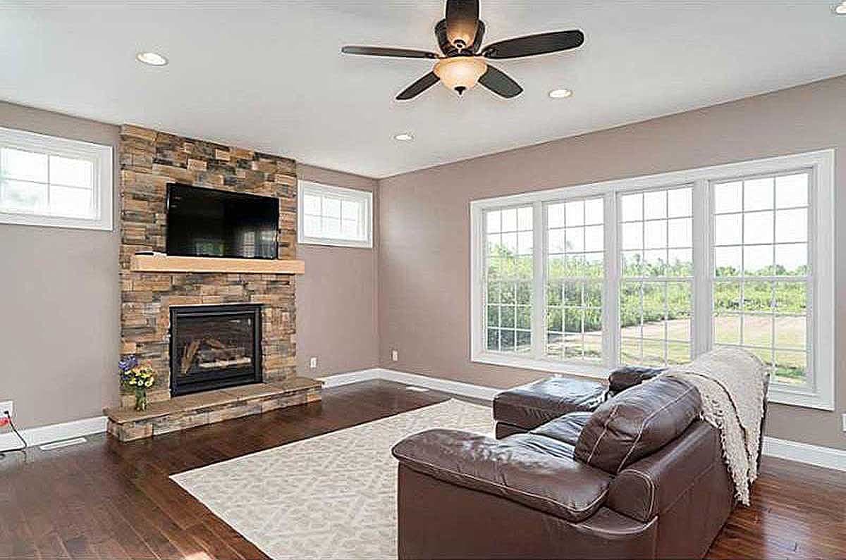 Living room with stone fireplace, mounted TV, hardwood floors, and large grid-pane windows.