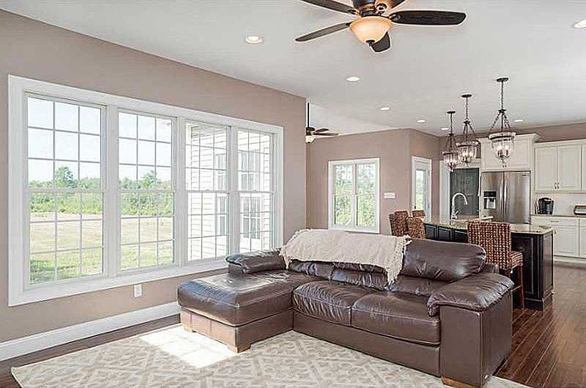 Open concept living area with large grid-pane windows, sectional sofa, and kitchen island with pendant lights.
