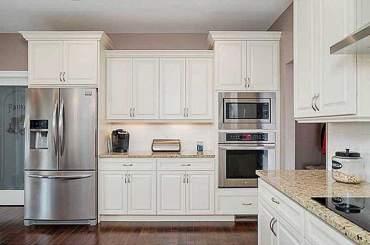 Kitchen with white cabinetry, stainless steel refrigerator, built-in microwave and oven, and granite countertops.
