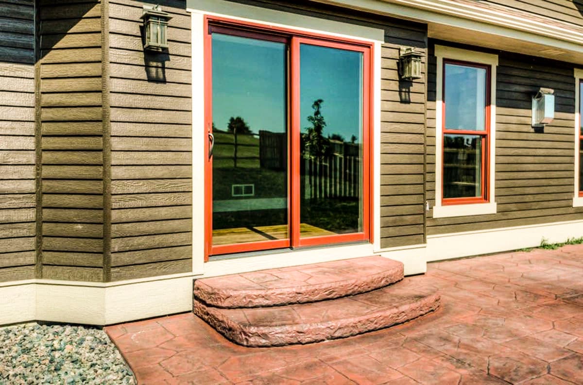 House plan exterior with horizontal siding, red-trimmed sliding glass doors, and two-tiered stone steps.