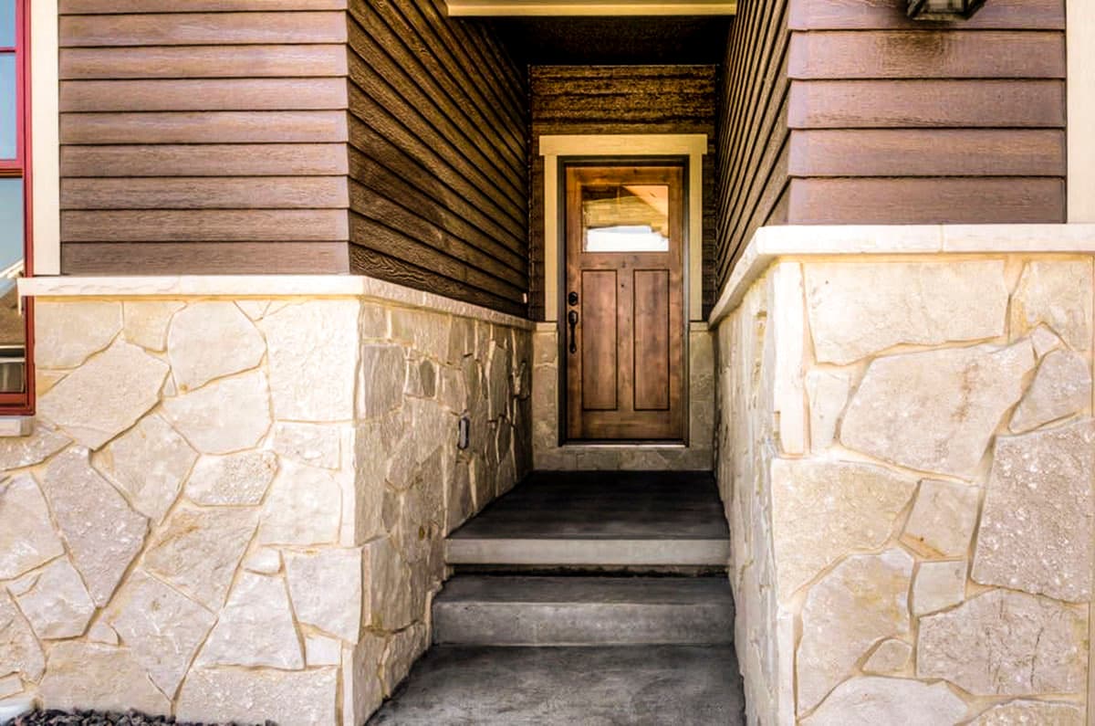 House plan exterior: entrance with wood door, stone base, and horizontal siding.