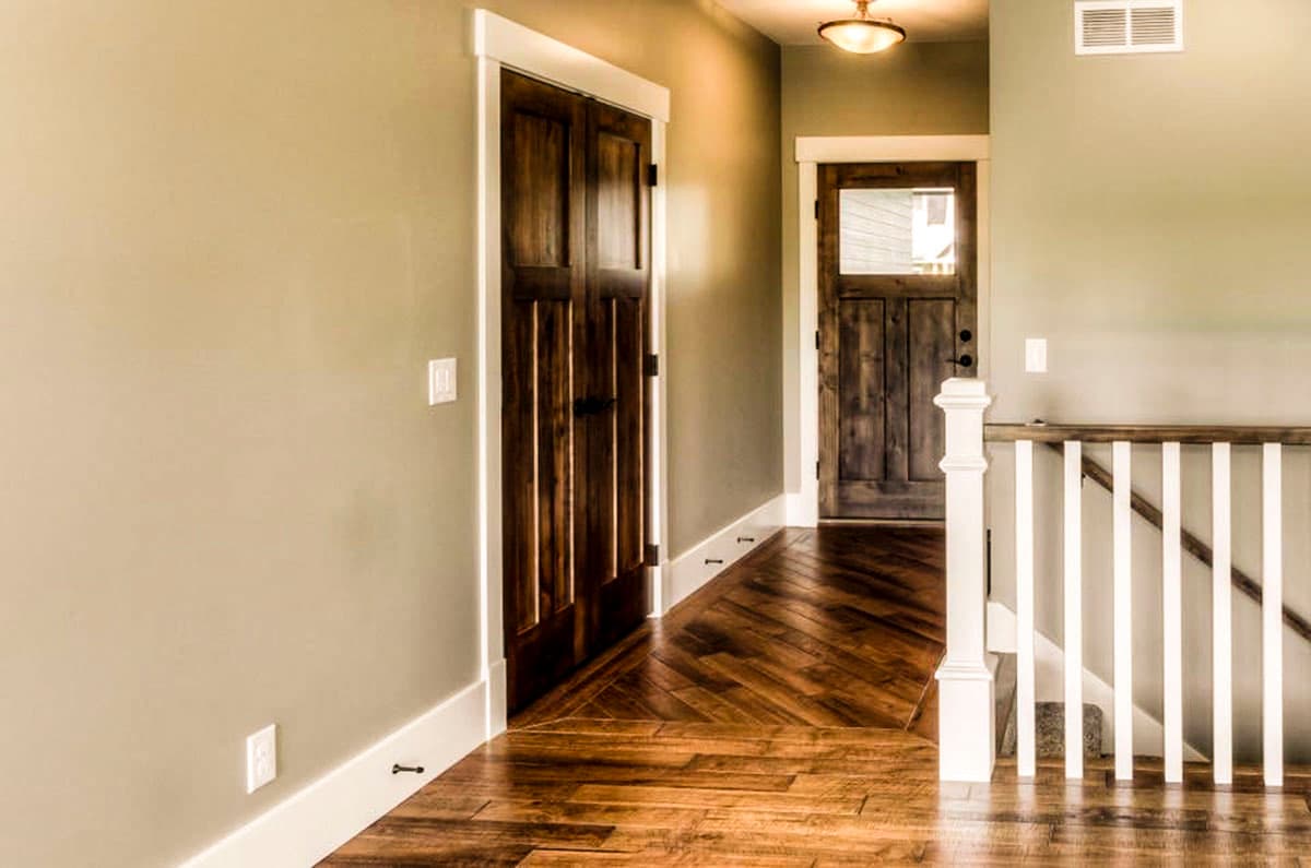 Interior view of a hallway with double wooden doors, a single door with a window, and a staircase with white balusters.