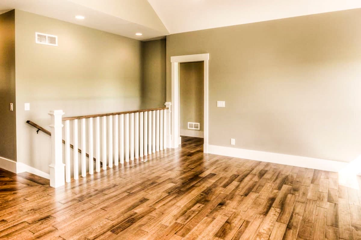 Interior view of a hallway with hardwood floors, white spindle railings, and a doorway to another room.