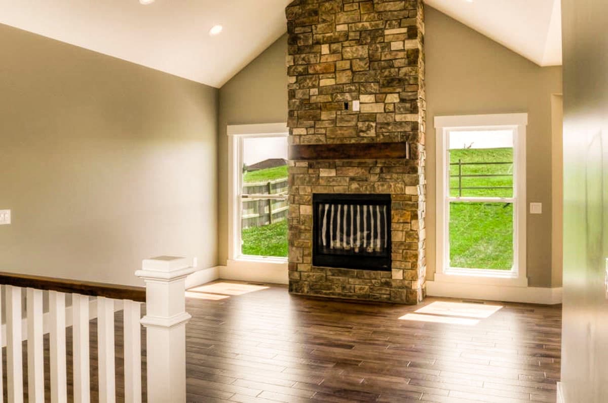 Interior view of a living room with vaulted ceiling, stone fireplace, wood floor, and white railing.