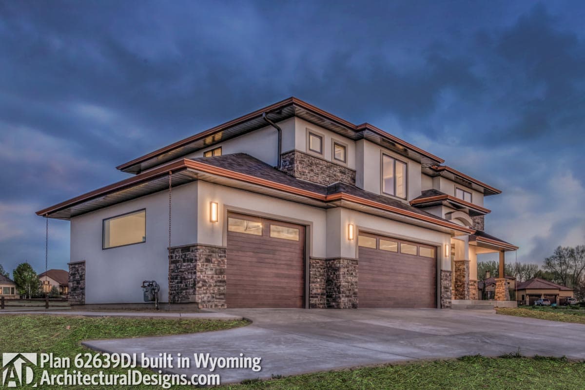 Modern house plan exterior with a four-car garage, stacked stone accents, deep eaves, and multi-level rooflines.