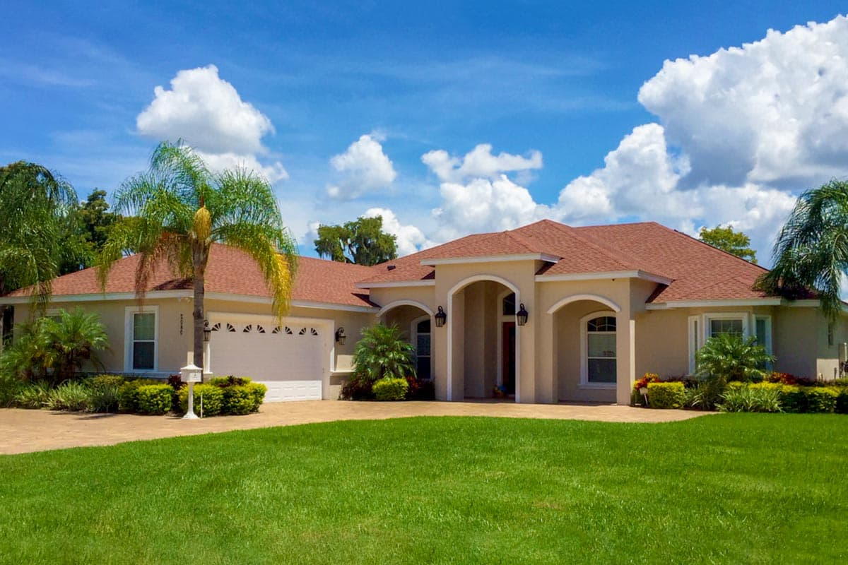 House plan exterior: one-story home with attached garage, arched entry, and tiled hip roof.