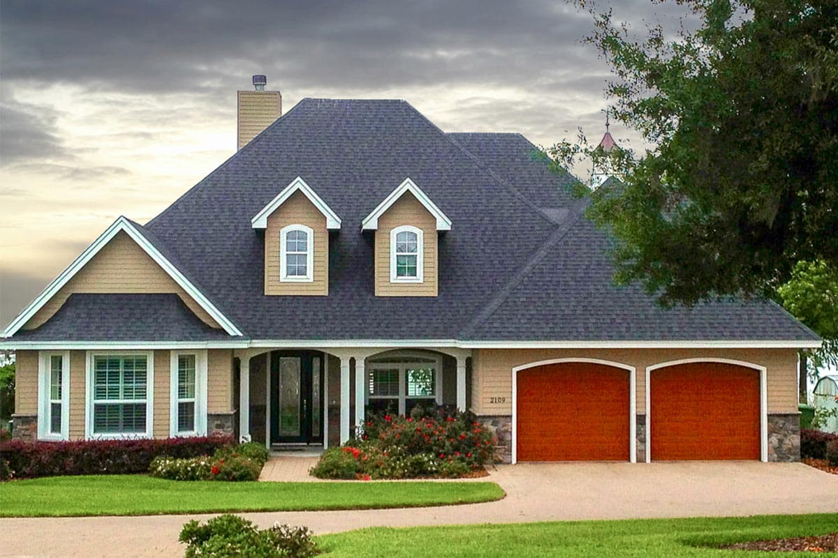 House plan exterior: Two-story Modern Farmhouse with dual gables, dormers, stone accents, and a three-car garage.