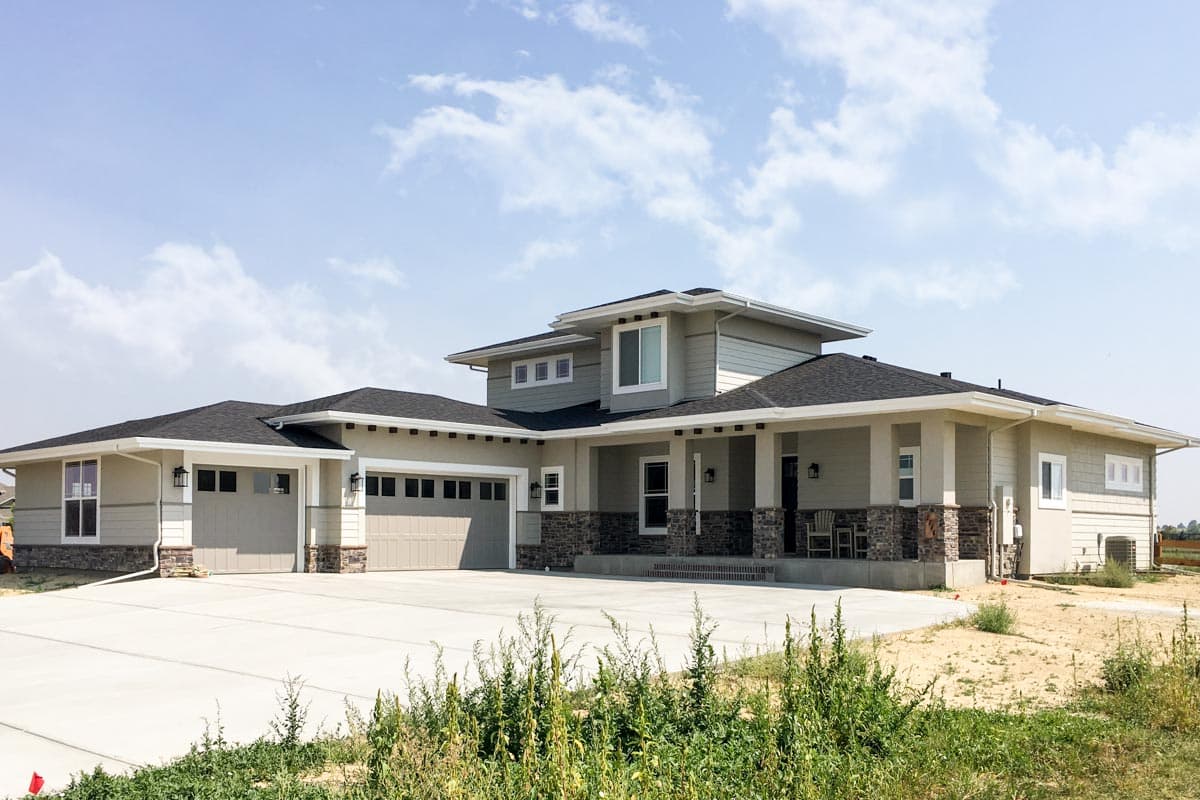 House plan exterior: Modern style, one and a half stories, with a covered porch, three-car garage, and stone accents.