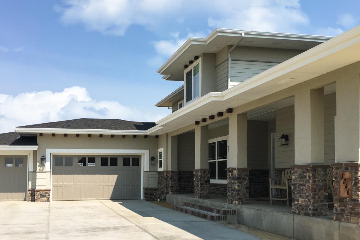 House plan exterior with a covered porch supported by stone-clad columns, wide eaves, and a two-car garage.