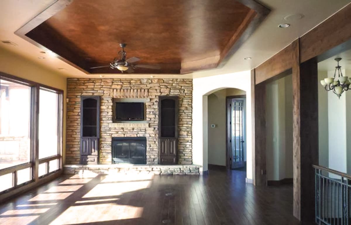 Interior view of great room with stone fireplace, built-in cabinets, tray ceiling, and large windows.