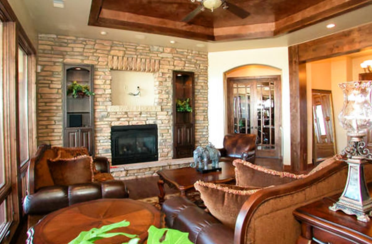 Living room with stone fireplace, wood-paneled ceiling, leather furniture, and double doors.