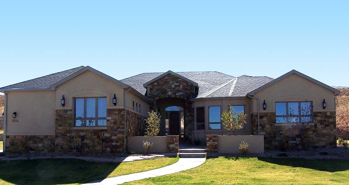 House plan exterior. Single-story, stucco and stone facade, with a prominent arched entryway and multiple gables.