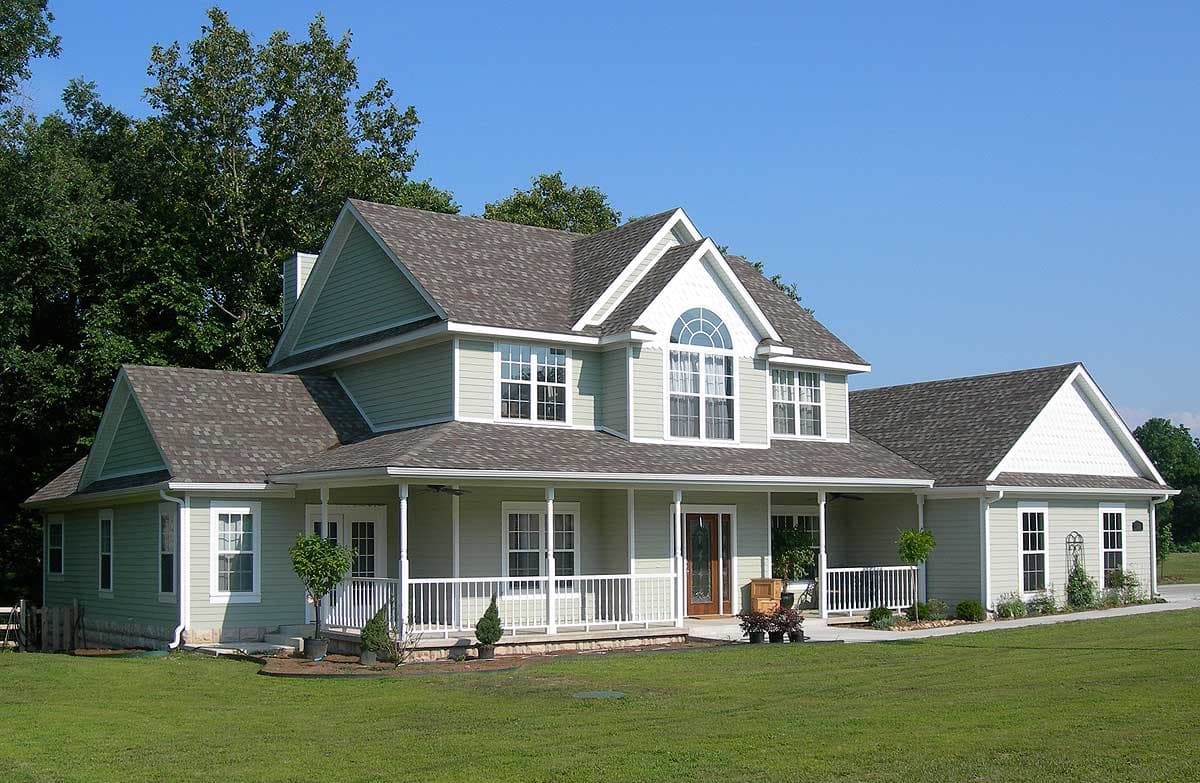 House plan exterior: Two-story home with wrap-around porch, gabled dormers, and arched window.