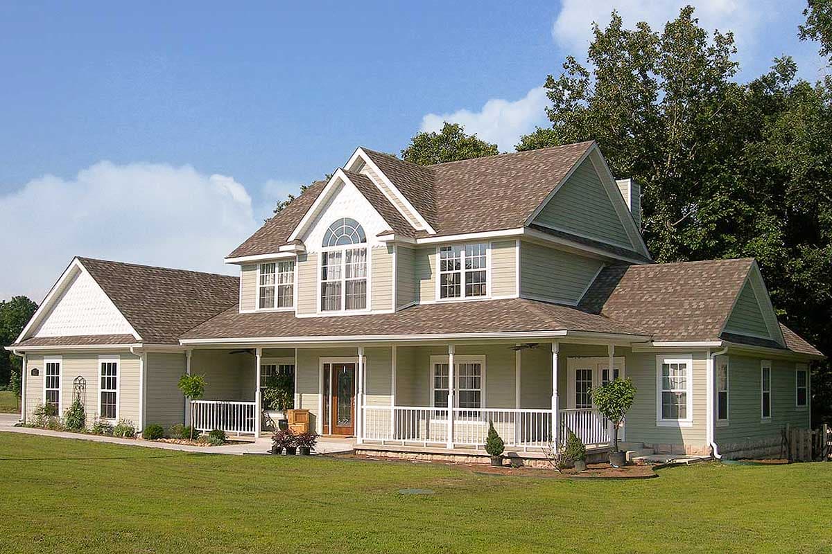 House plan exterior: Two-story home with a wraparound porch, prominent gables, dormer windows, and an arched window above the entrance.