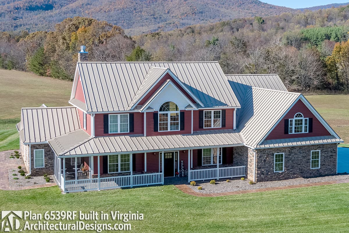 House plan exterior: Two-story dwelling with a wrap-around porch, stone foundation, gable dormers, and metal roof.