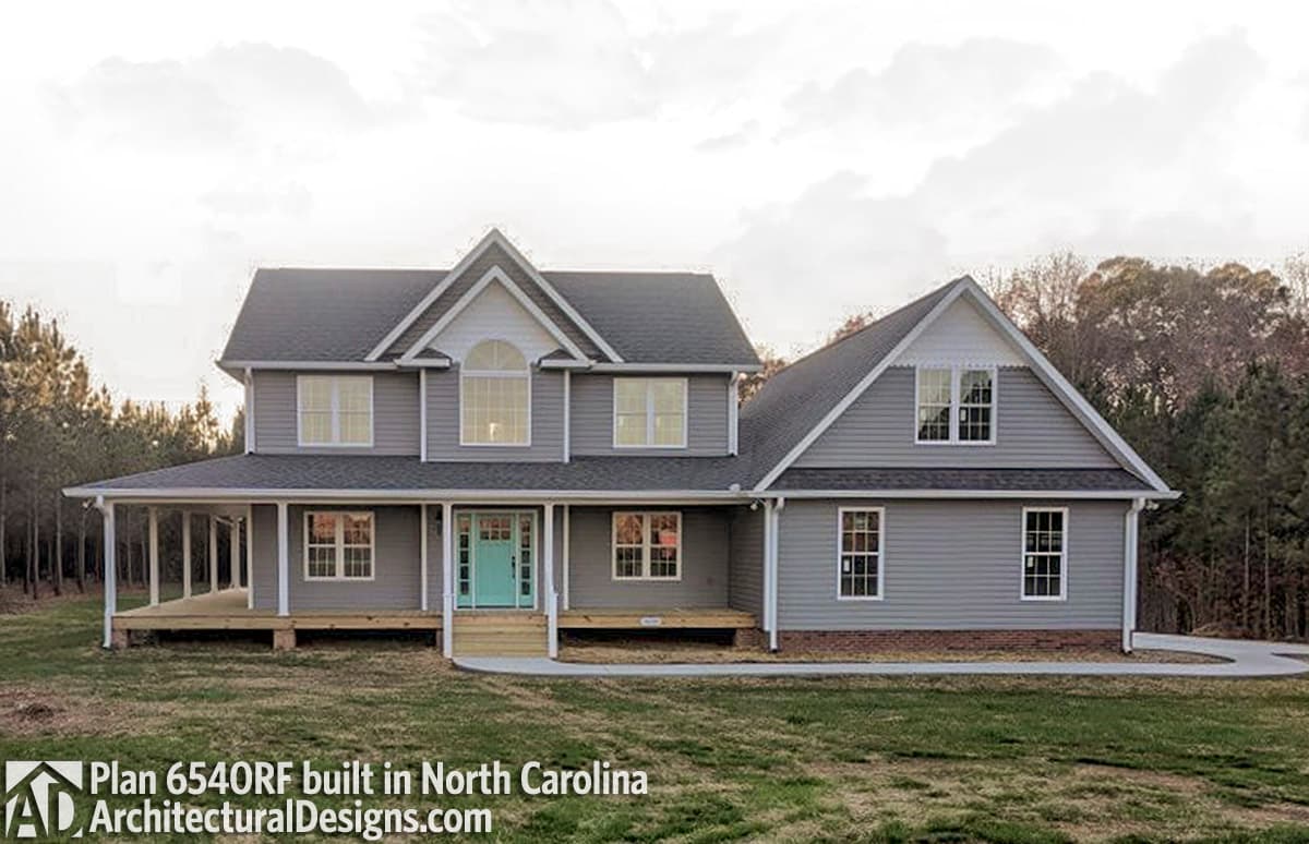 Two-story house plan exterior with a wraparound porch, gables, dormers, and arched upper window.