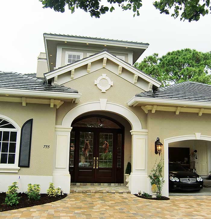 House plan exterior featuring arched entryway with double doors, gabled rooflines, and attached two-car garage.