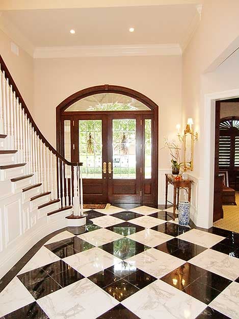 Foyer with curved staircase, arched double doors with glass panes, and black and white marble floor.