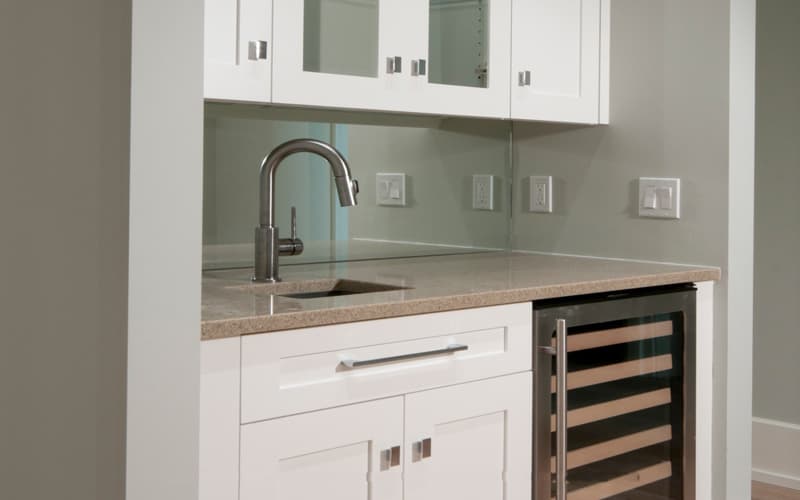 Bar area with white cabinets, granite countertop, stainless steel faucet, sink, and wine cooler.