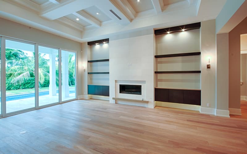 Living room with coffered ceiling, fireplace, built-in shelving, and sliding glass doors leading to a pool area.