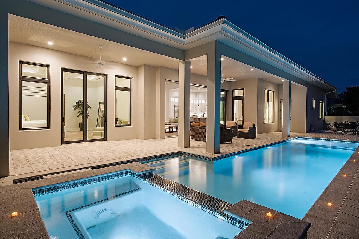 Modern house exterior with covered patio, multiple levels of pool and spa, and large glass doors.