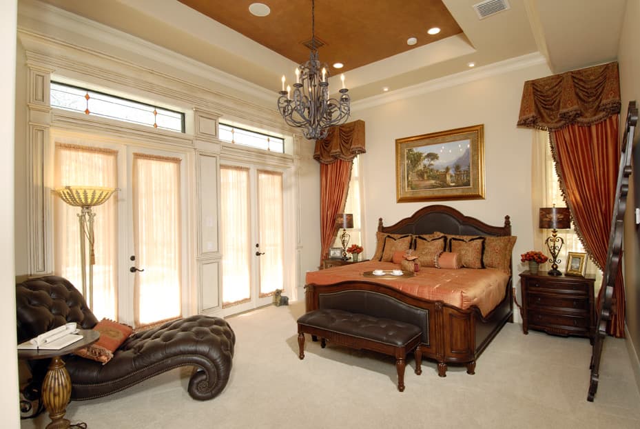 Bedroom interior with king size bed, tufted chaise lounge, and French doors with transom windows.