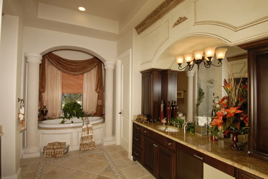 Bathroom with arched alcove containing corner bathtub, columns, and draped window. Vanity with double sinks and dark wood cabinetry.