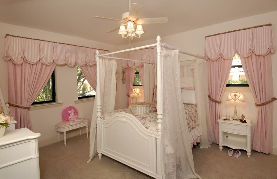 Bedroom with white canopy bed, pink striped valances with scalloped trim, and white nightstand.