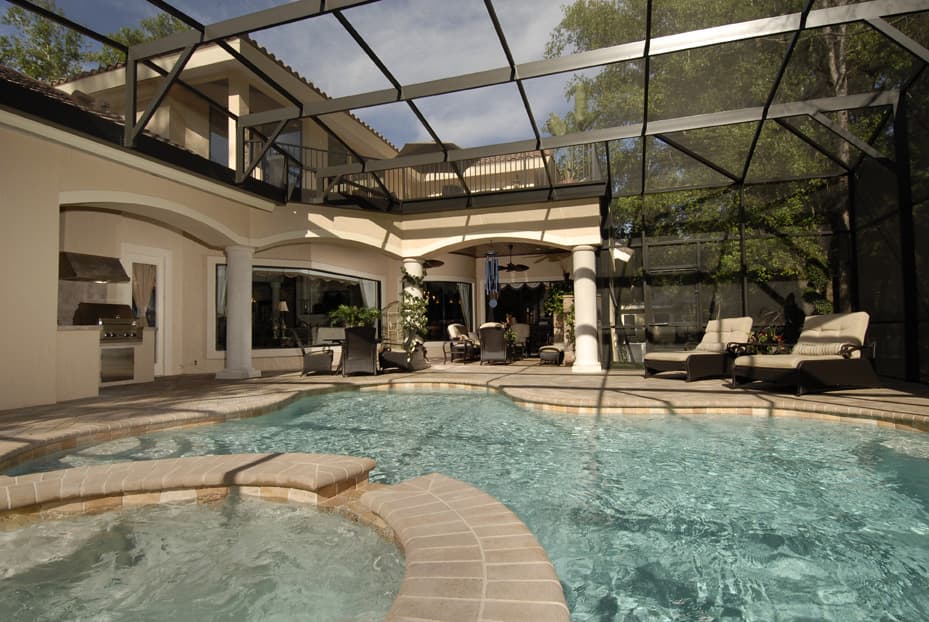 Covered patio with built-in grill, pool, spa, and second-story balcony, all enclosed by a screened lanai.
