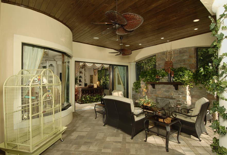 Covered patio with stone fireplace, seating area, wood-paneled ceiling with ceiling fans, and sliding glass doors.