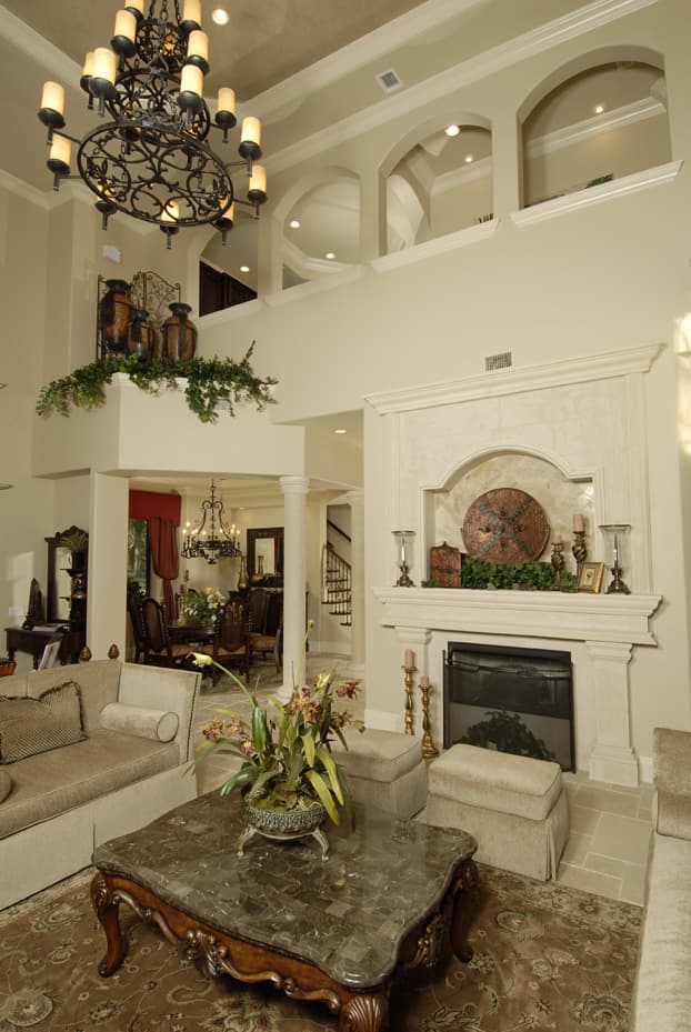 Interior rendering of a living area with a two-story fireplace, arched openings to a dining room, and a large chandelier.