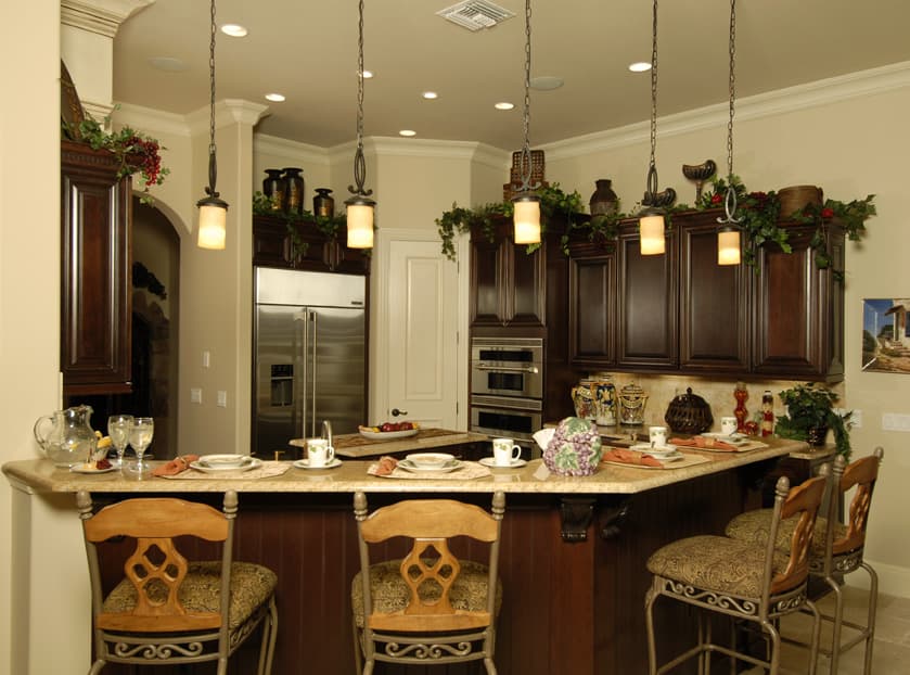 Kitchen island with dark wood cabinetry, granite countertops, stainless steel refrigerator, ovens, and pendant lighting.