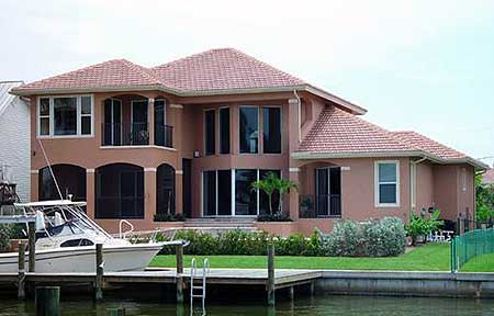 House plan exterior: two-story, red tile roof, multiple gables, large windows, and a small balcony.