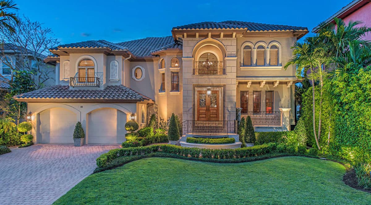 House plan exterior: Two-story Mediterranean style with a tiled roof, arched entryway, balconies, and a three-car garage.