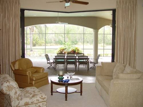 Interior view of a living room with large windows leading to an outdoor dining area and pool.