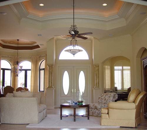 Interior view of a grand entryway with double doors, arched windows, tray ceilings, and decorative columns.