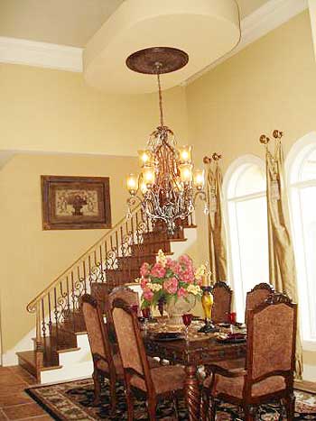 Dining room with a large table, ornate chandelier, and a wrought-iron staircase.