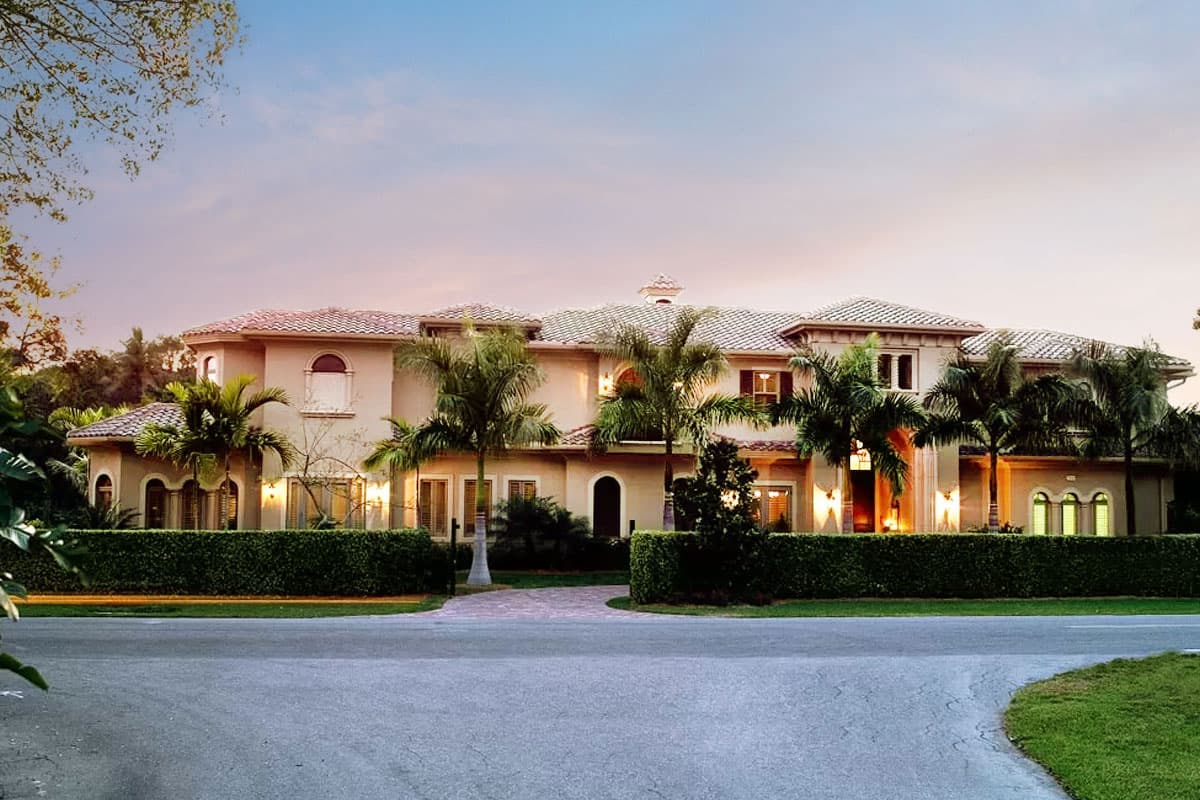 Two-story house plan exterior with a stucco finish, tile roof, arched windows, and manicured hedges.