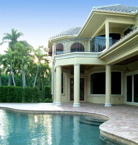 Exterior view of a two-story house with a second-story balcony, covered patio with columns, and a tiled roof.