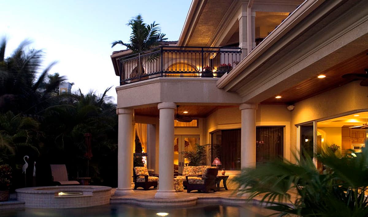 House plan exterior with second-story balcony, columns, and covered patio with seating.