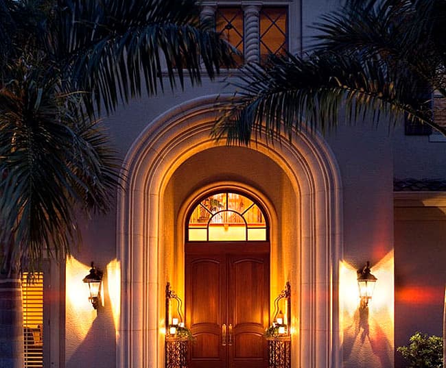 Exterior house plan: Grand arched entryway with double wooden doors, arched transom window, and decorative sconces.