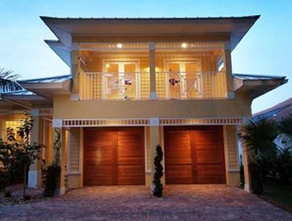 House plan exterior showing a two-story home with a second-floor balcony, double garage doors, and distinctive rooflines.