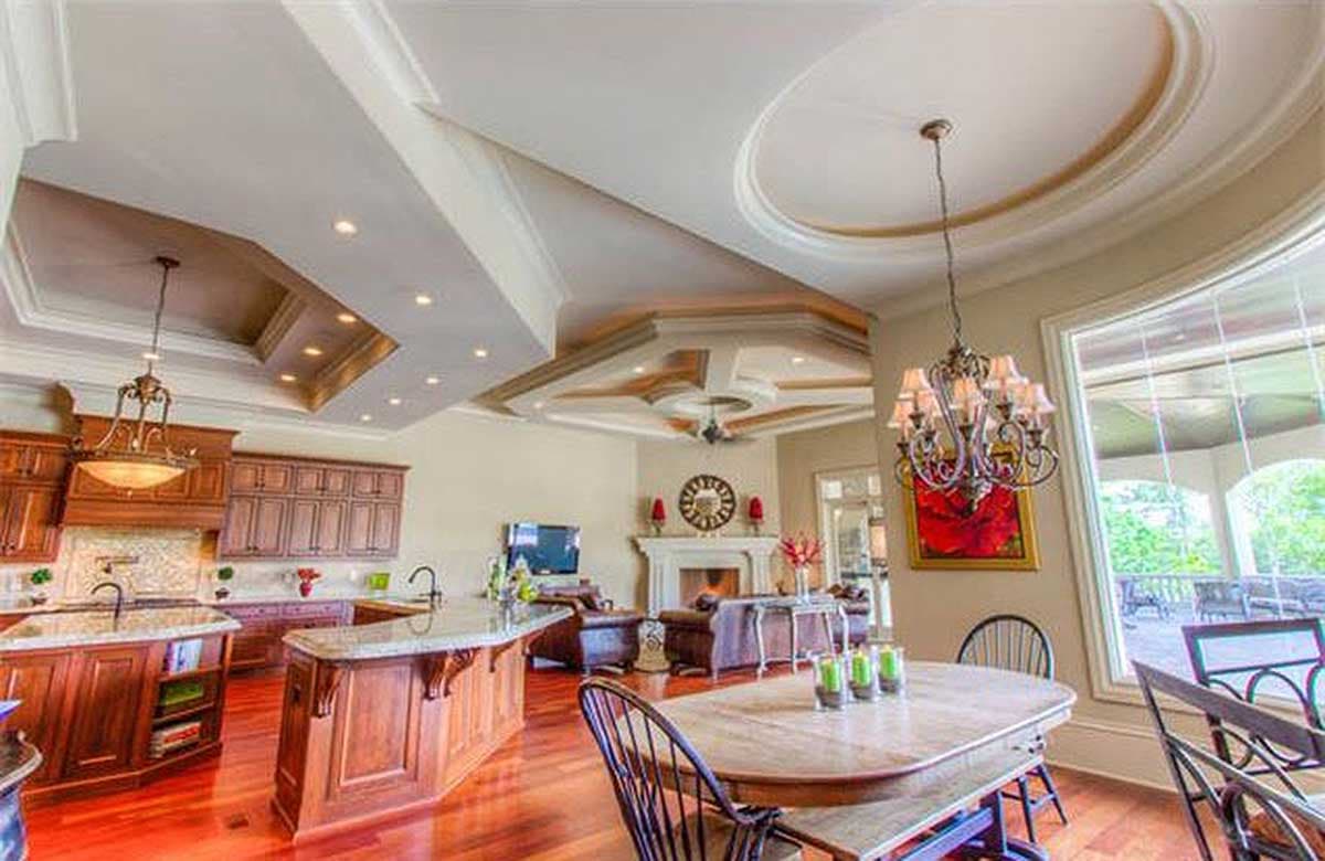 Interior view of a kitchen and great room with an open layout, two islands, coffered ceilings, and a fireplace.