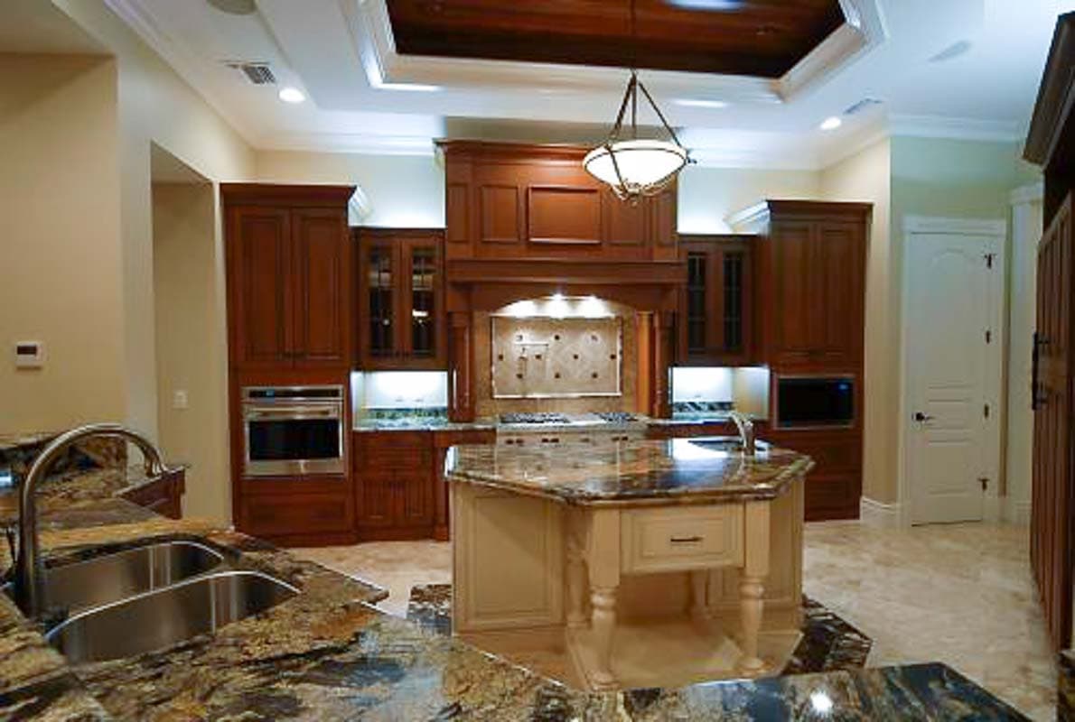 Kitchen featuring custom wood cabinetry, a central island with granite countertop, built-in ovens, and a decorative range hood.