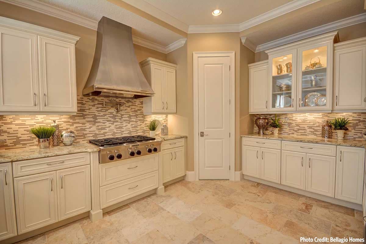 Kitchen featuring cream cabinets, granite countertops, stainless steel range hood and backsplash with mosaic tile.