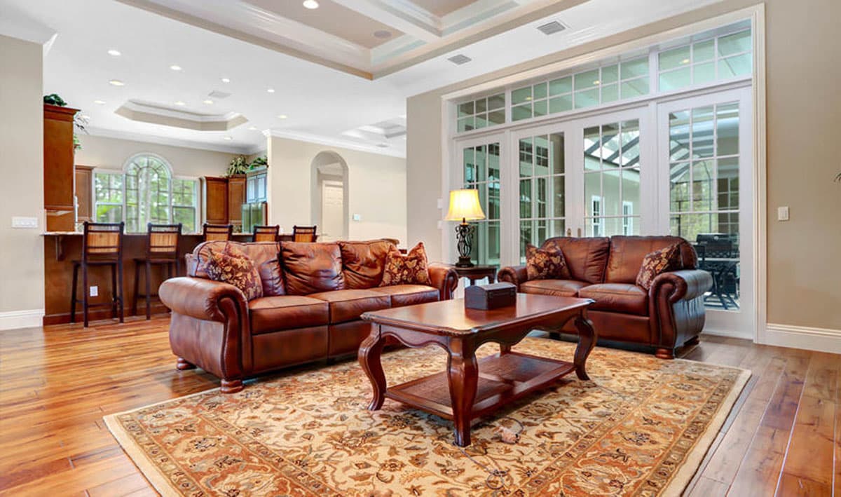 Living room with leather sofas, ornate rug, dark wood coffee table, and a bar area with stools.