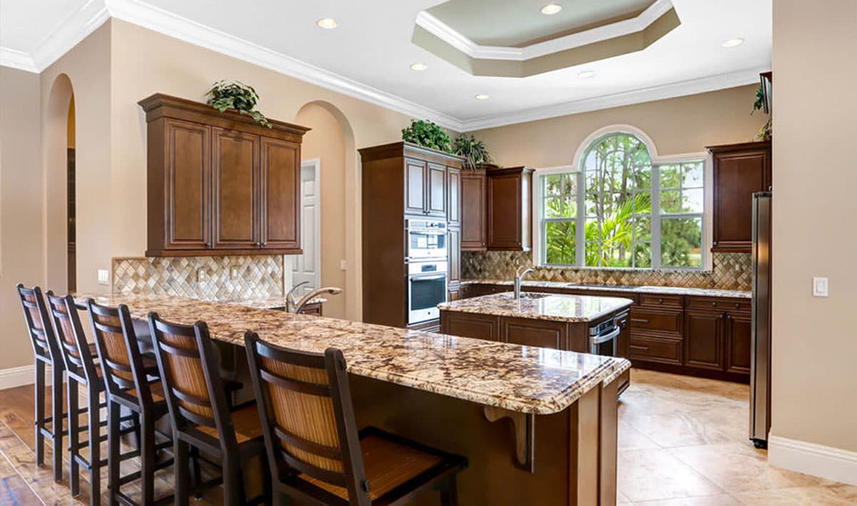 Kitchen with dark wood cabinetry, granite countertops, large island with seating, and arched window.