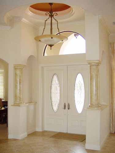 House plan interior entry: double doors with oval glass, arched transom window, recessed ceiling with chandelier, and decorative columns.