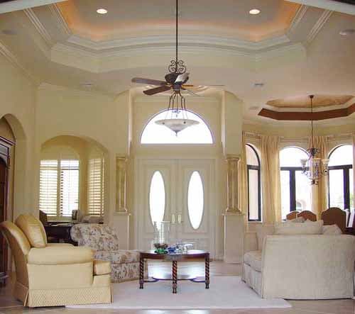 Interior view of a grand foyer with double doors, arched windows, a coffered ceiling, and ornate lighting fixtures.