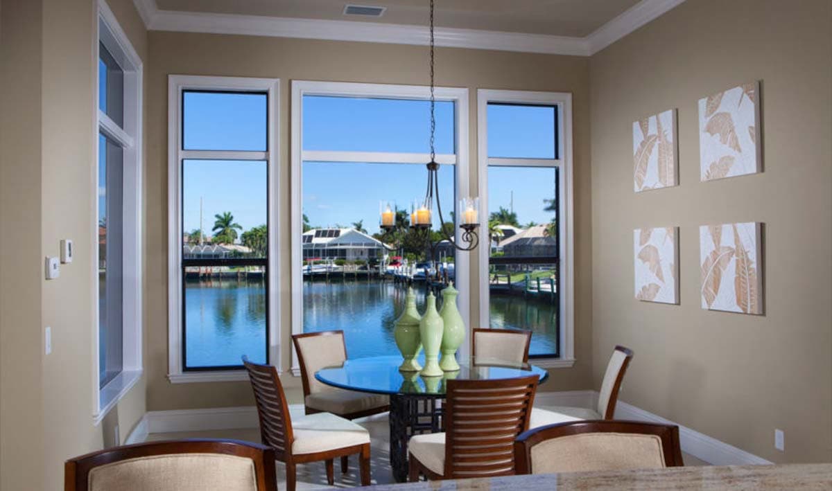 Dining area with a glass-top table and chairs, overlooking a canal with houses and boats.